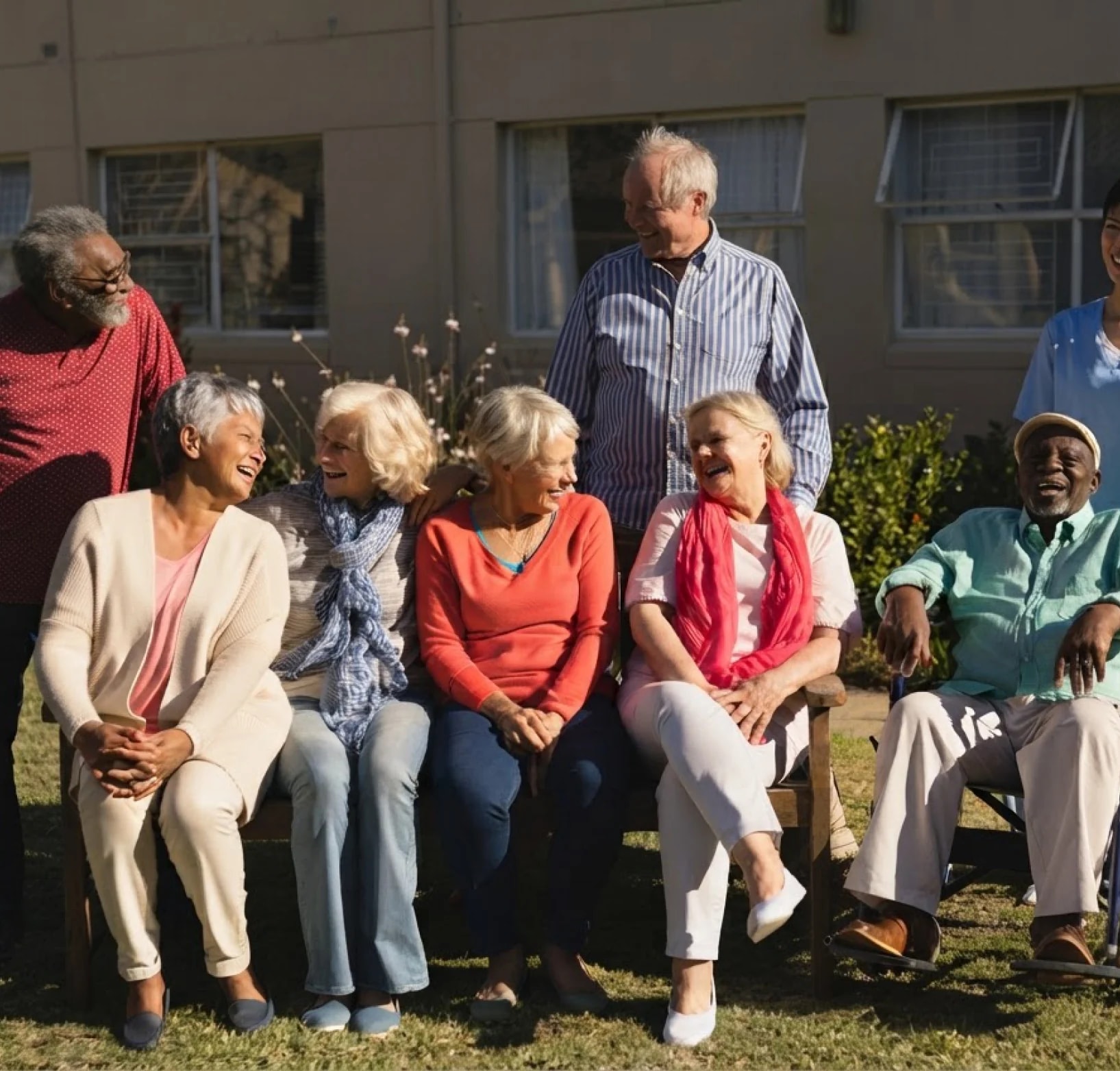 A group of older adults laughing together in a sunny garden.