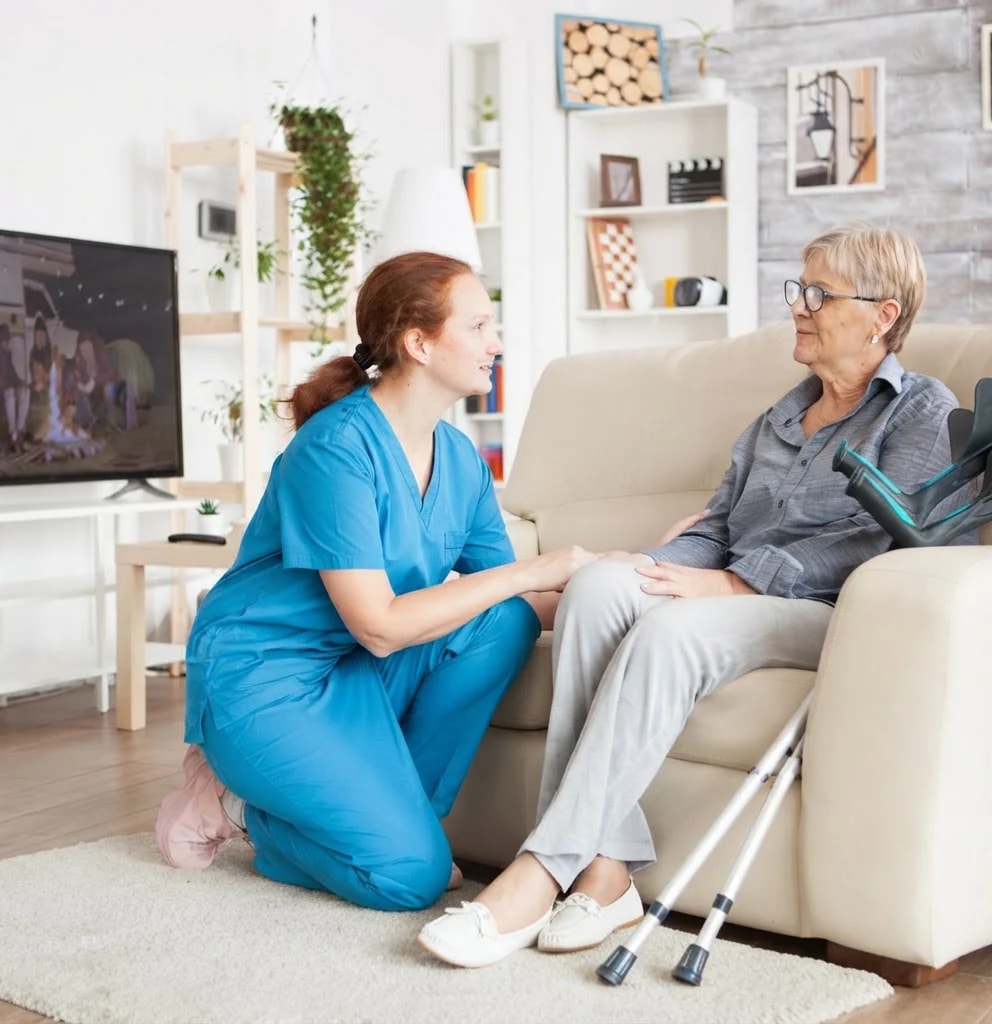 A nurse crouching beside an older woman in her living room.