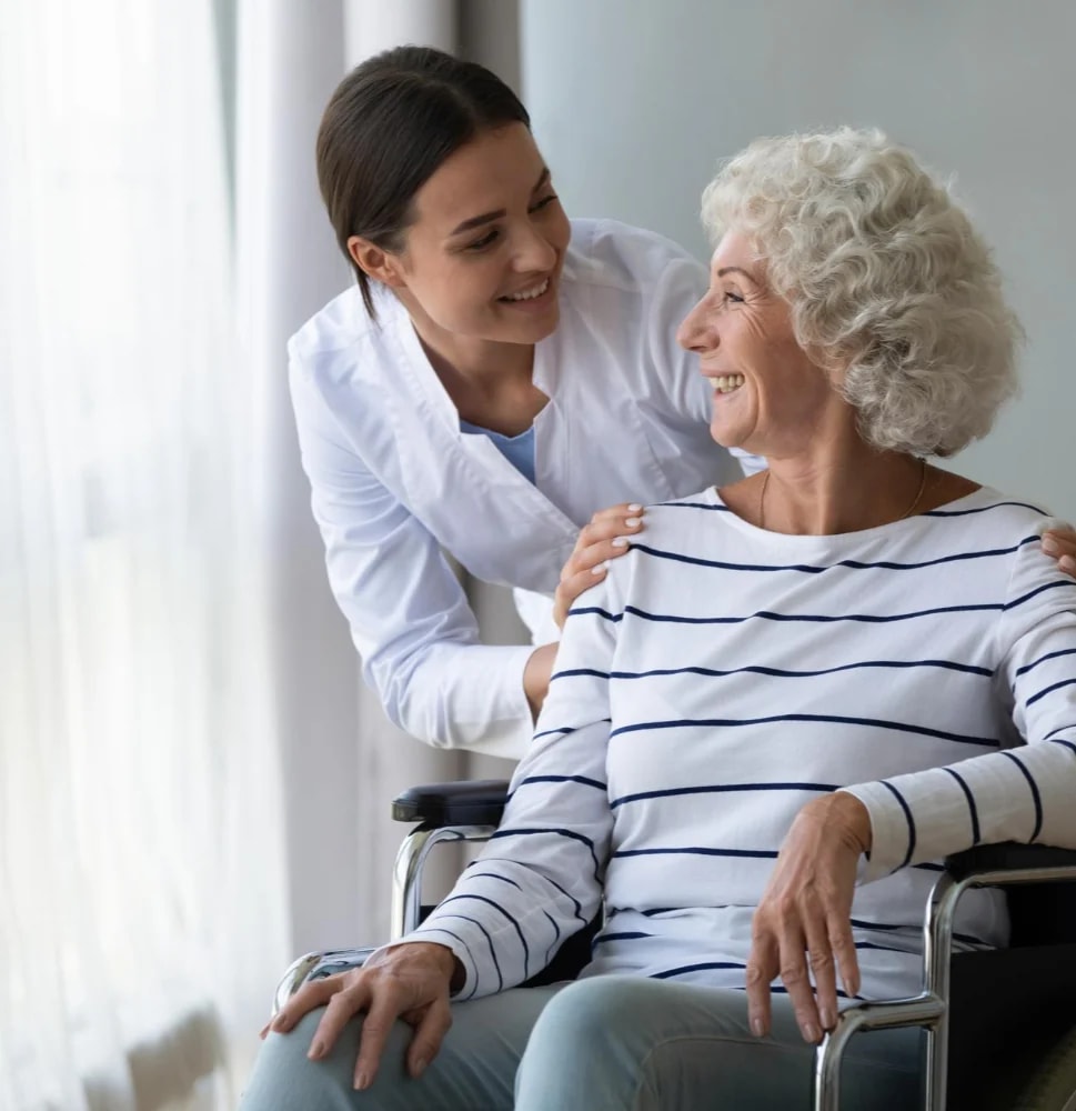 A carer with her hand on the shoulder of a woman in a wheelchair.