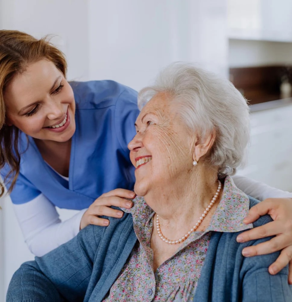 A carer leaning in to talk with a smiling older woman.