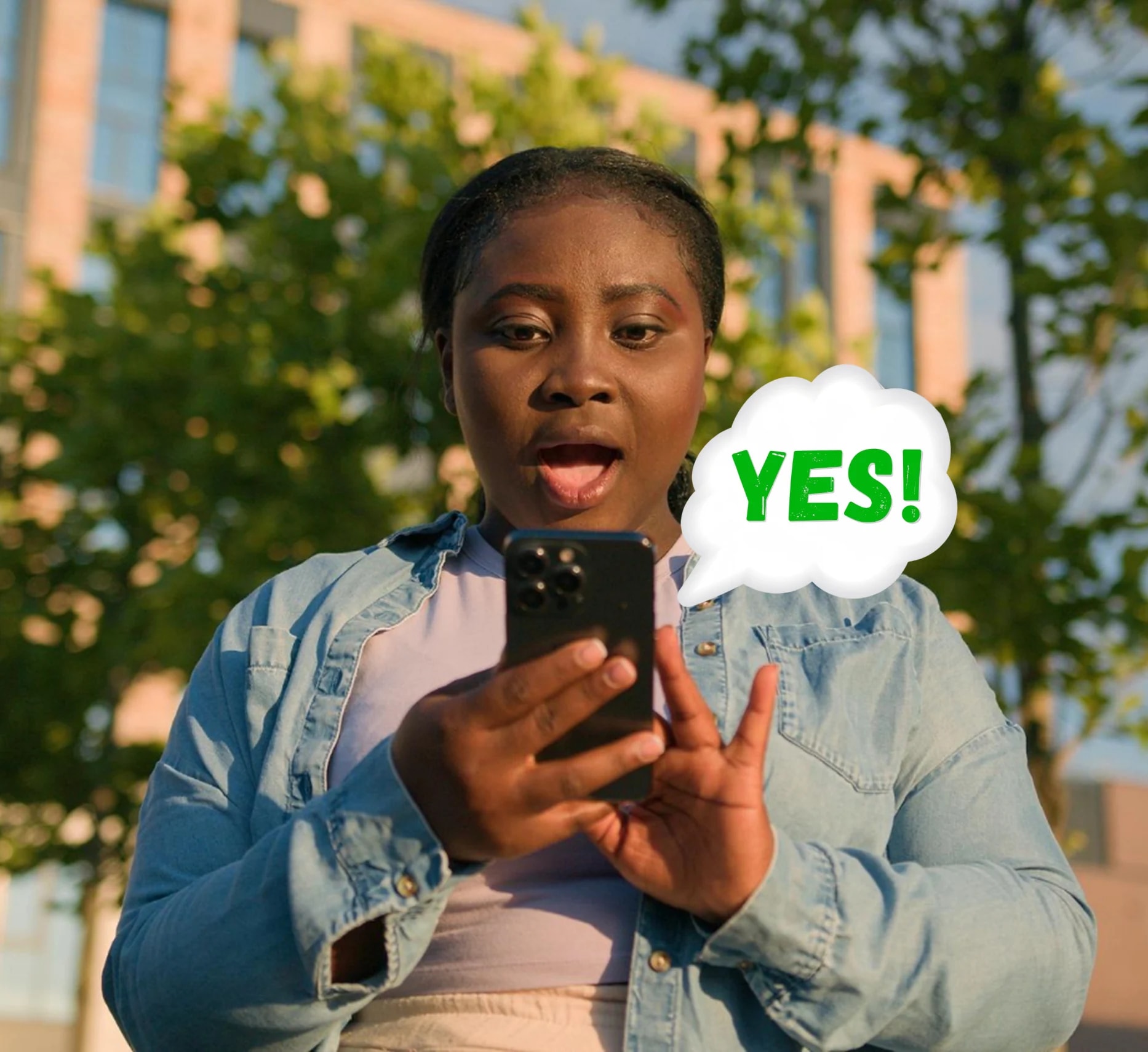 A woman smiling at her phone with a bright YES speech bubble beside her.
