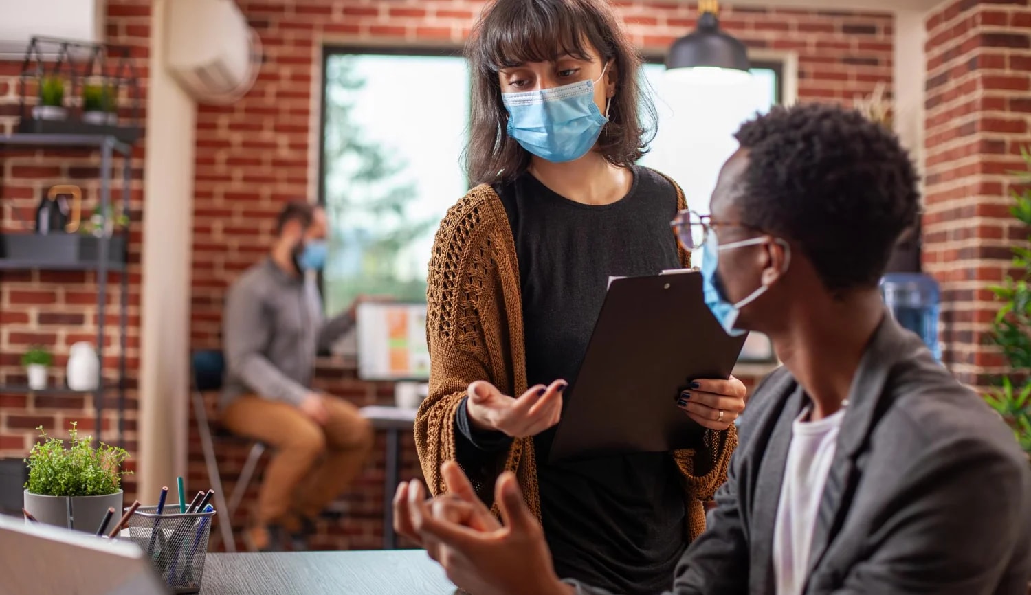 A manager with a clipboard briefing a colleague in a care setting.