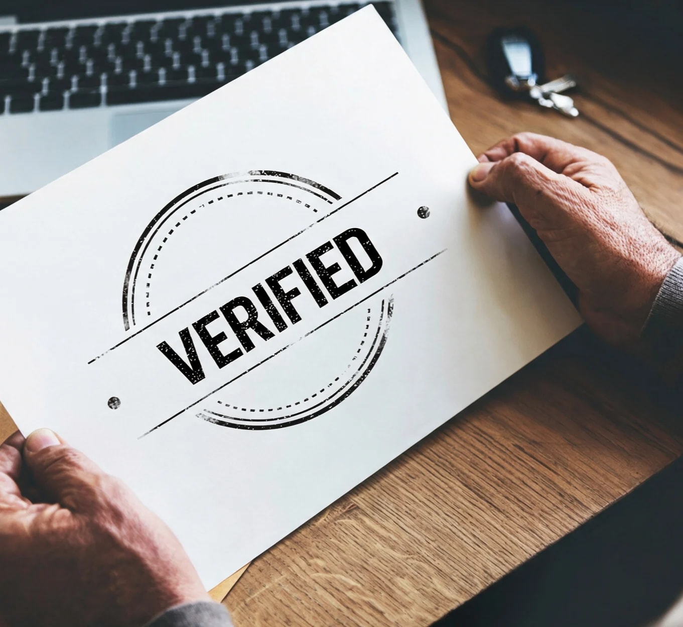 Hands holding a sheet of paper stamped VERIFIED.