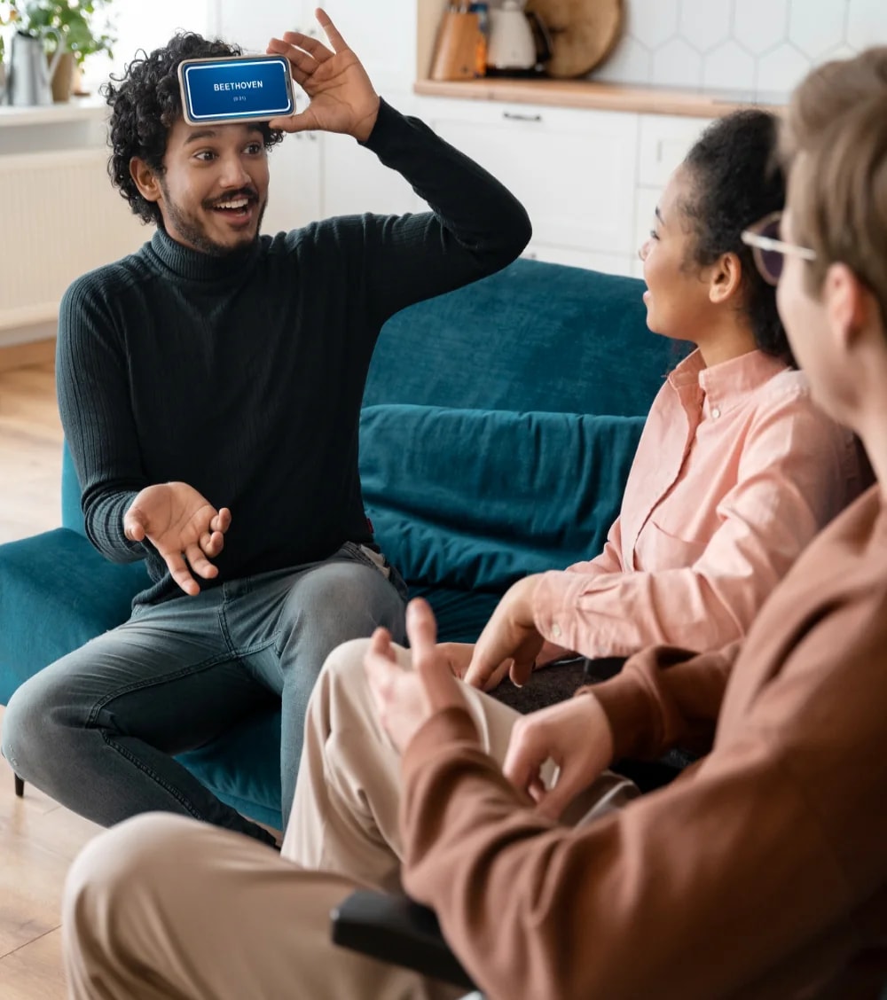 A man showing something on his phone to two women on a sofa.