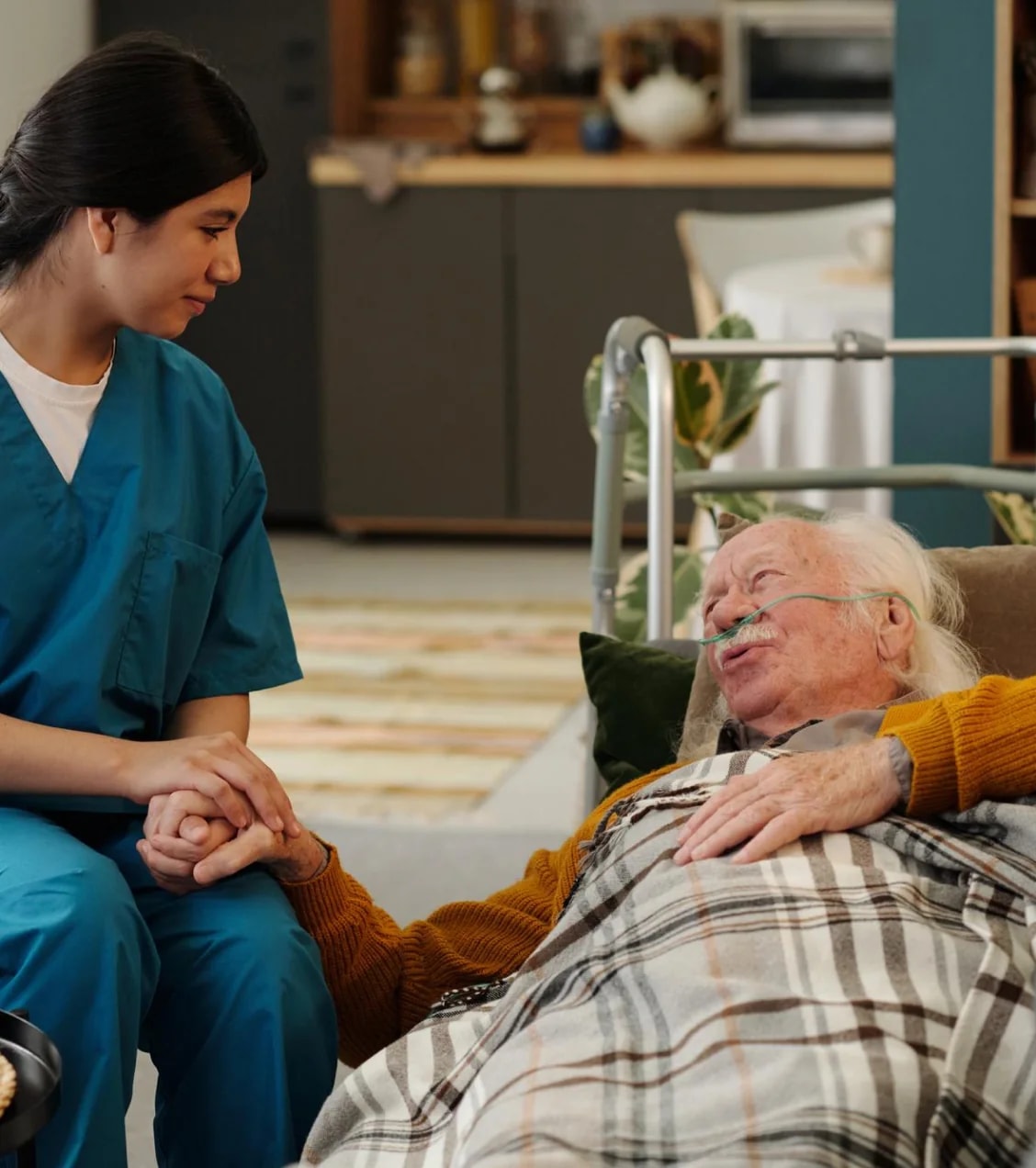 A nurse holding the hand of an older man resting in bed.