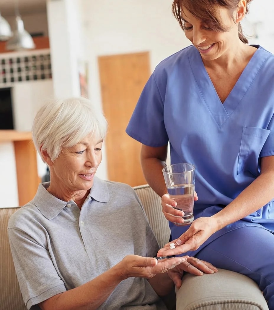 A carer handing tablets and a glass of water to an older woman.