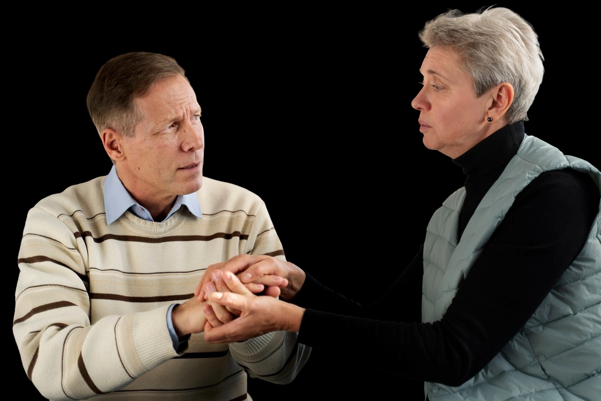 An older man and an older woman sitting together, holding each other’s hands.