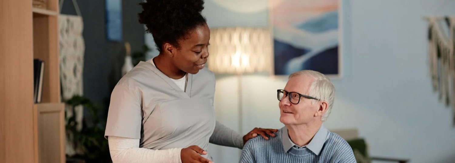 A carer sitting with an older man, checking a pulse oximeter together.