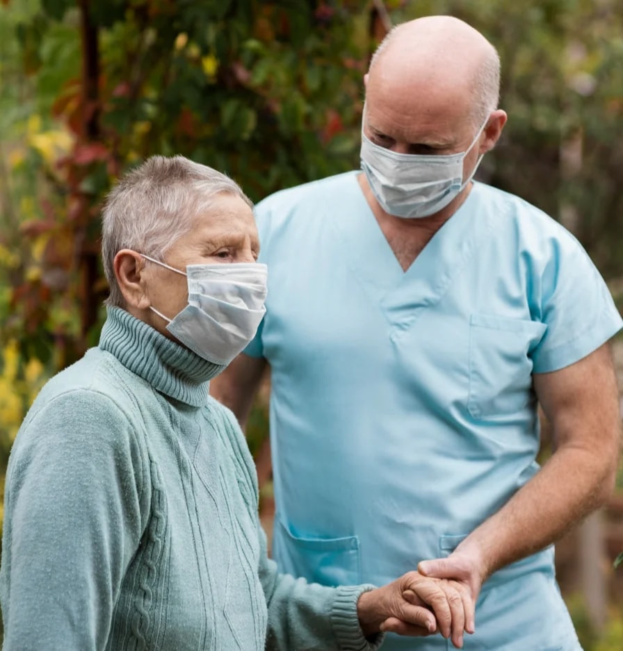A nurse walking arm in arm with an older woman in a garden.