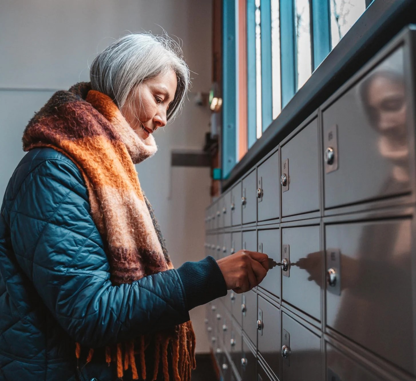 An older woman opening her box in a wall of post boxes.
