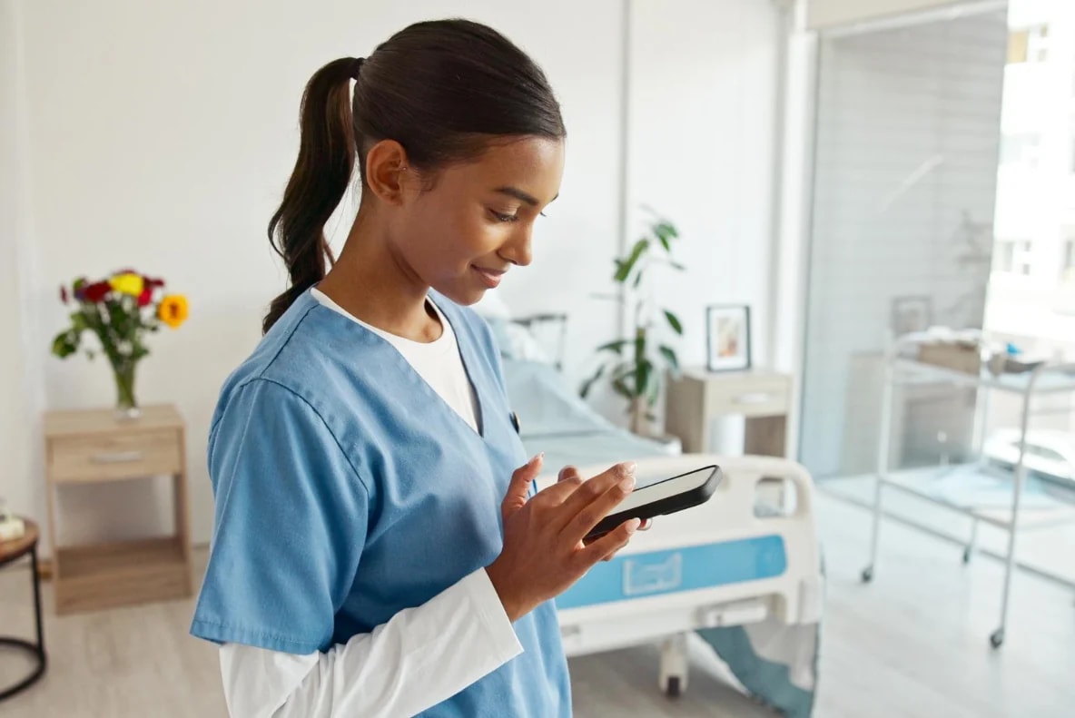 A nurse in blue scrubs checking her phone on a ward.