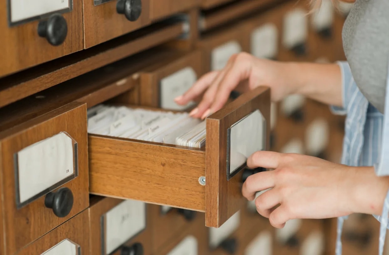 A hand opening a drawer in a wooden card index.