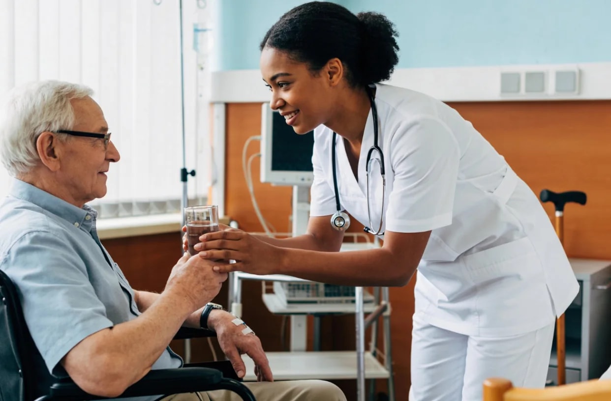 A nurse handing a glass of water and tablets to an older man.